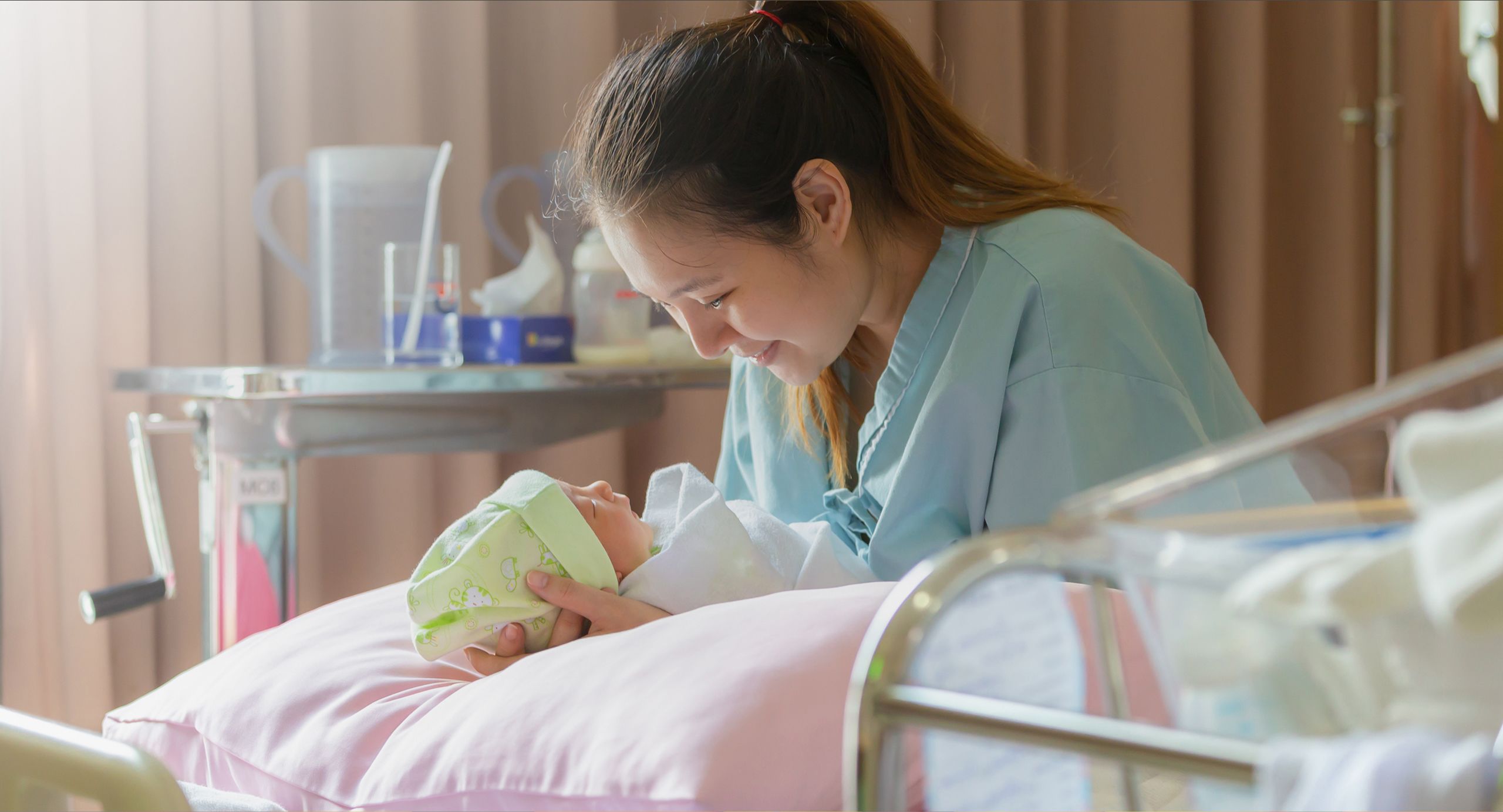 A mother smiling and holding a baby in a hospital bed.