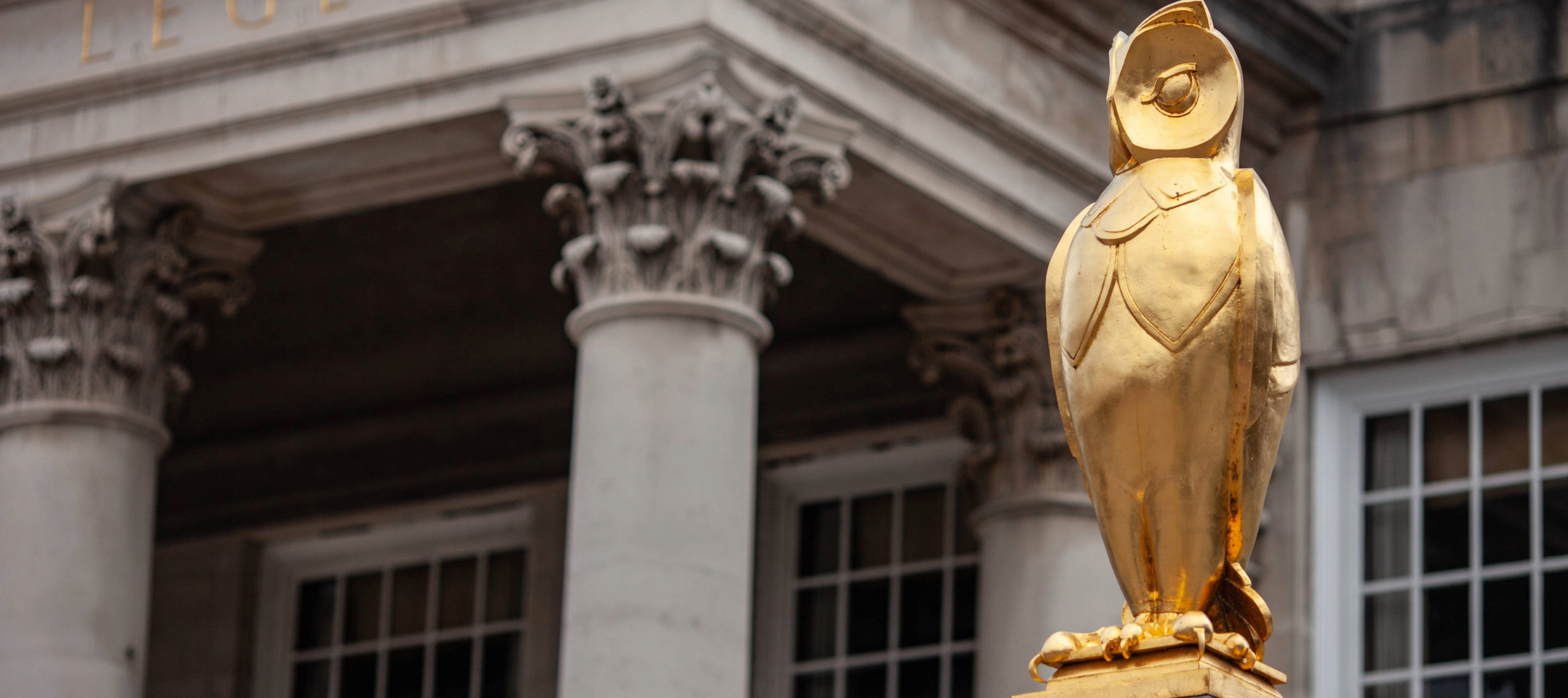 A golden owl statue stands in the foreground. Behind is a column of the Leeds City Council building.