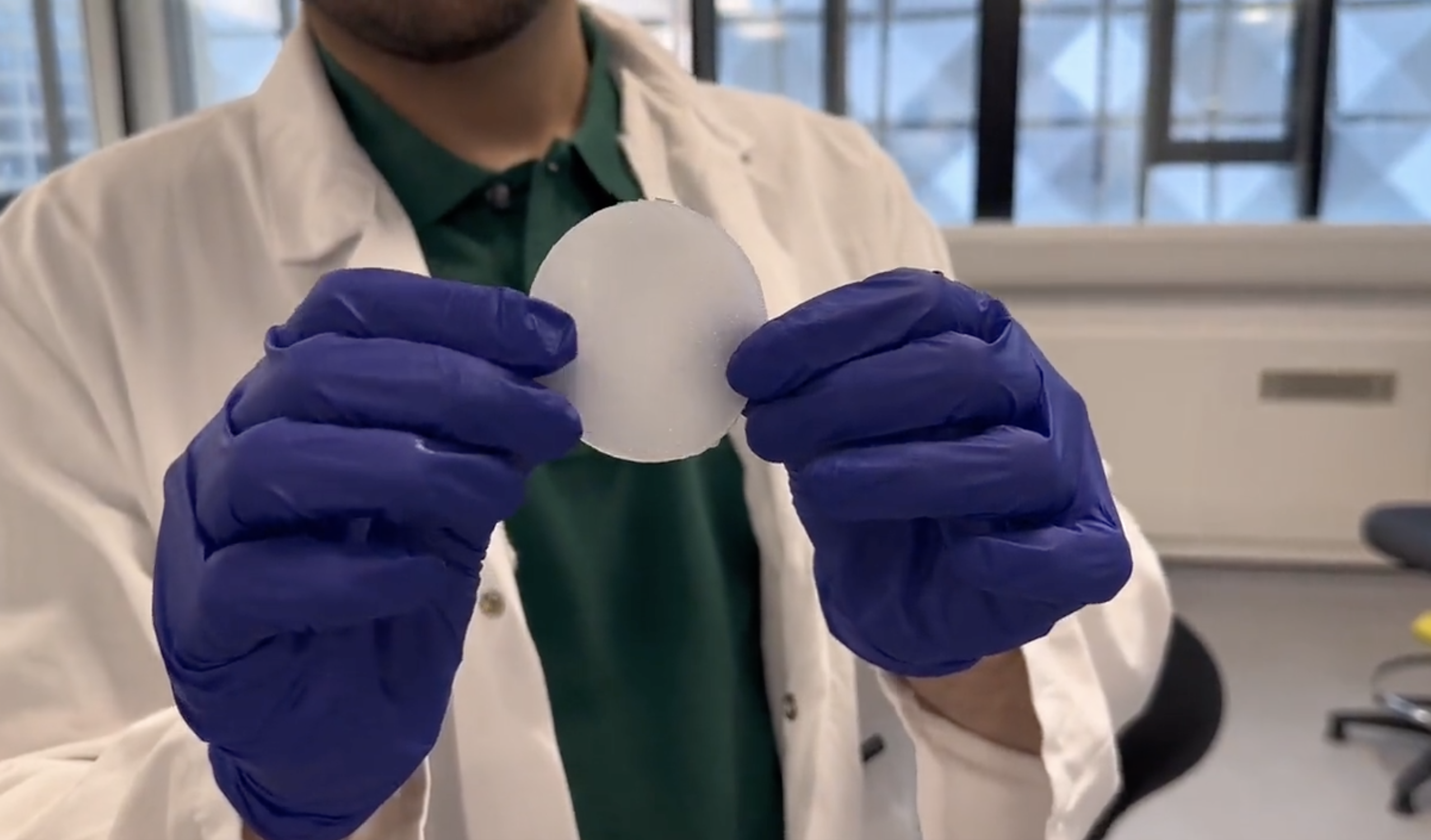 A person wearing a lab coat and gloves holding a 3D printed tongue simulator