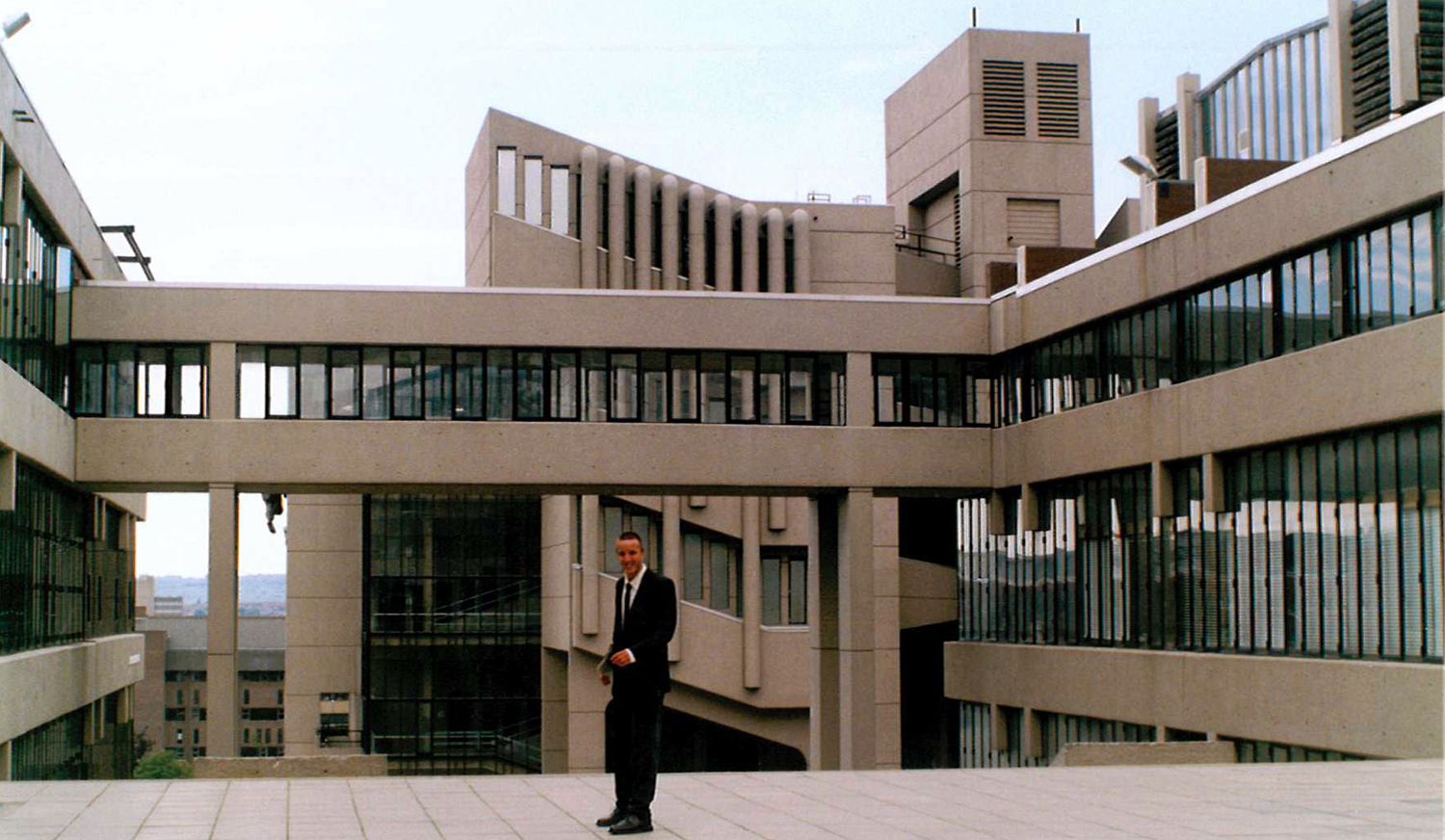 Man in suit standing in front of Brutalist buildings at University of Leeds