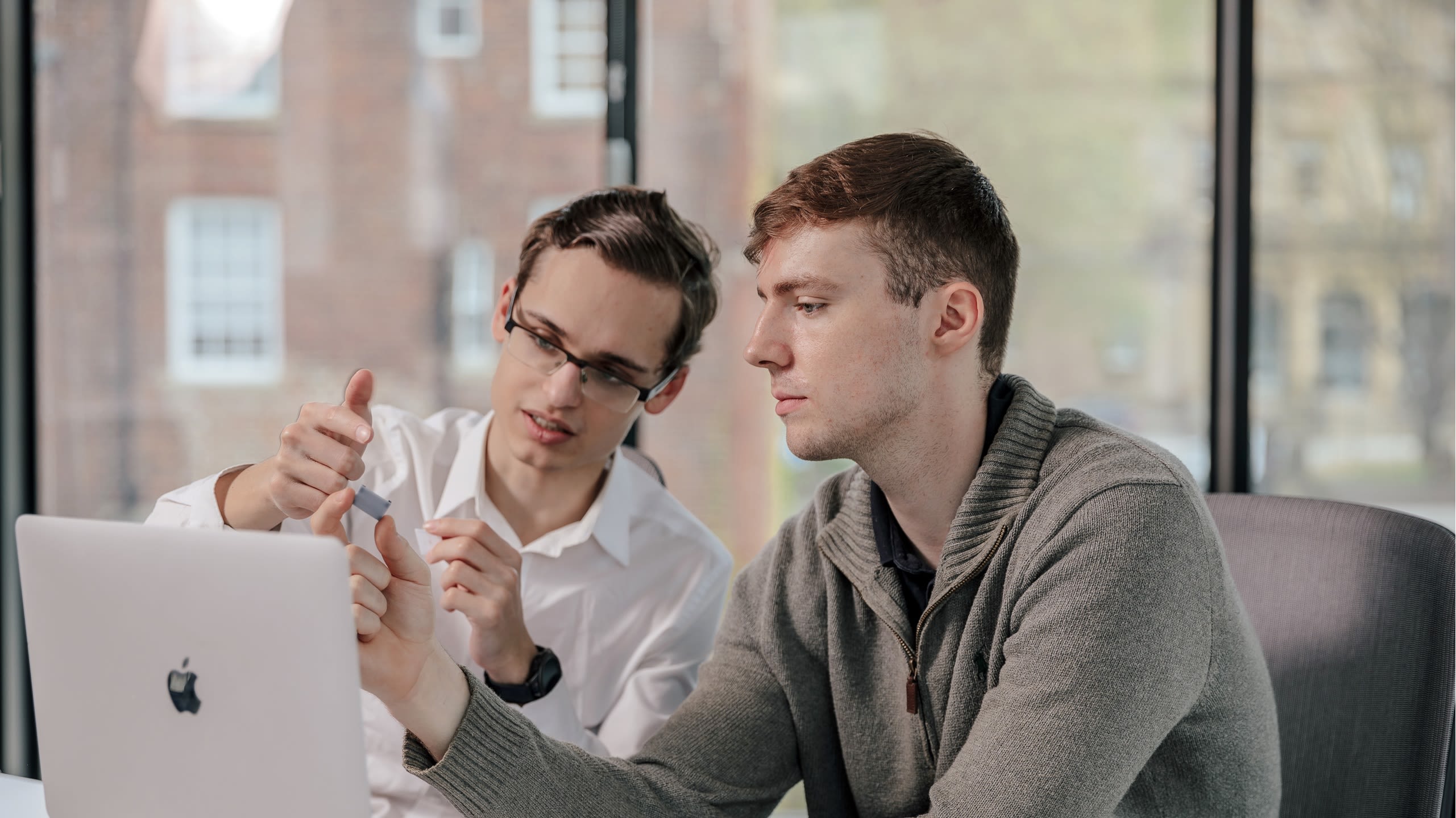 Ian and Henry, founders of Microneedle Solutions sit at a desk, both looking at the same laptop.