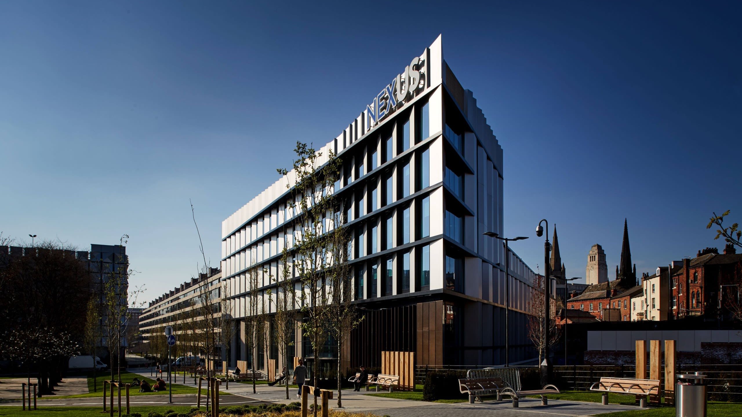 A photograph of the Nexus building taken from an angle. It is a tall, modern, white building with 'Nexus' signage on its face.