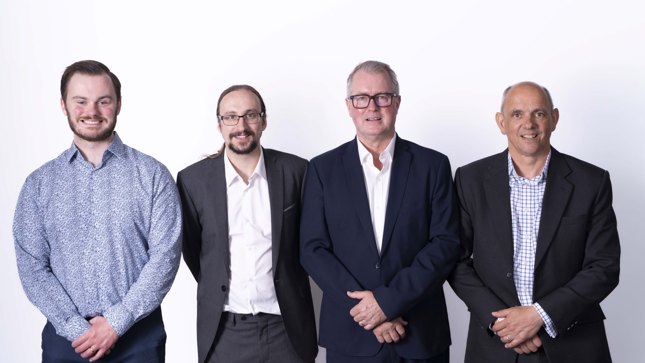 The founders of Auxetec stand smiling in a row, wearing formal dress, against a white background.