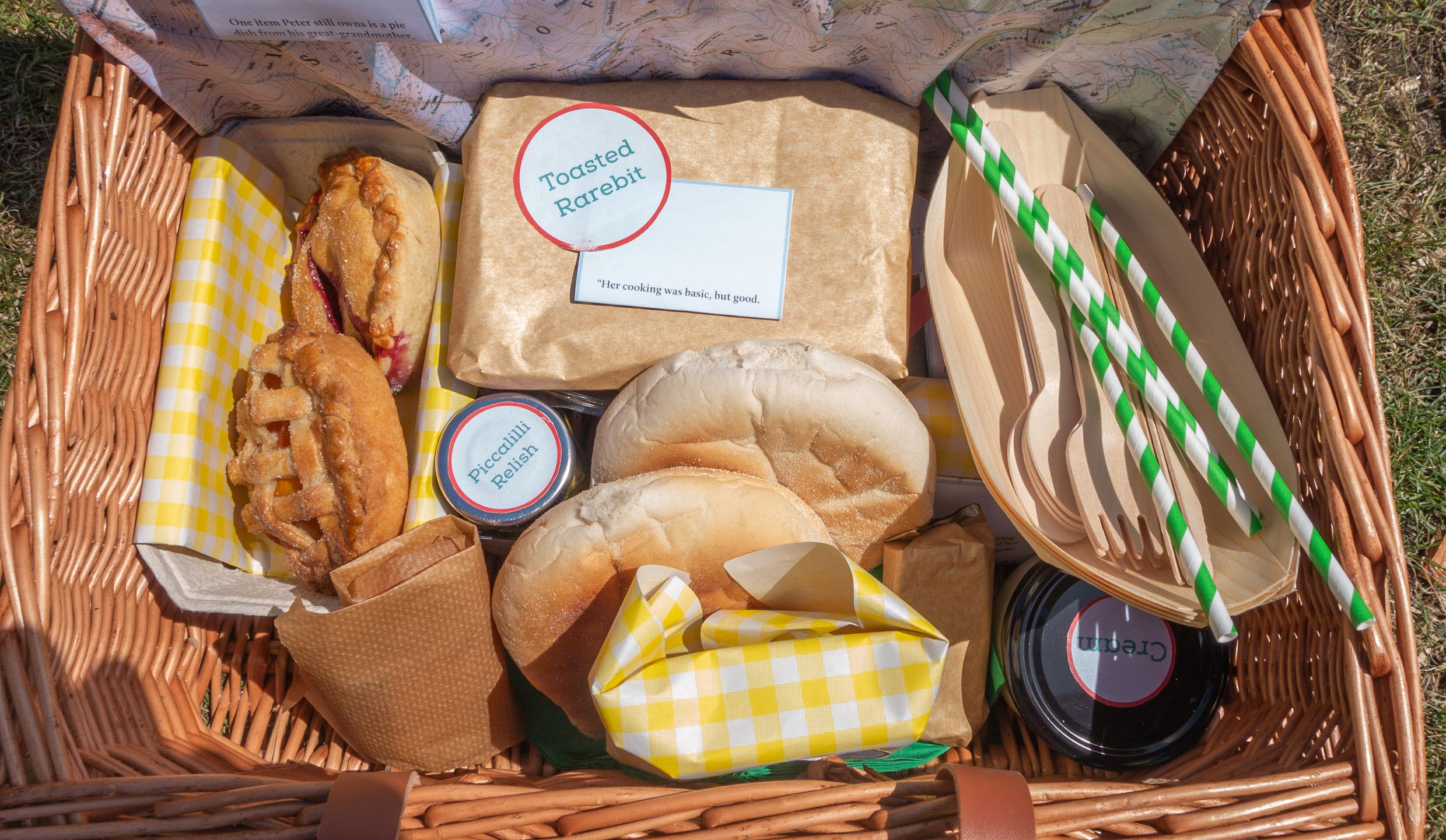 A picnic basket containing pasties, bread, toasted rarebit, picalilli relish, cream and straws.