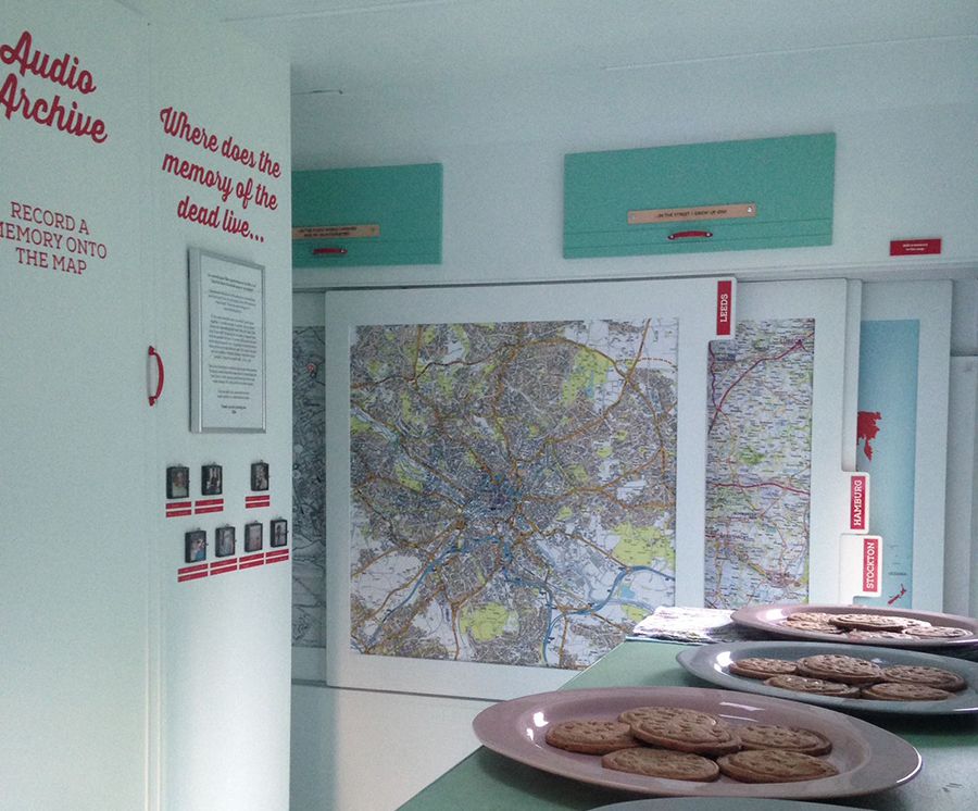 Maps displayed on the wall of the inside of the caravan, plates of biscuits and a wall display asking 'Where does the memory of the dead live?'