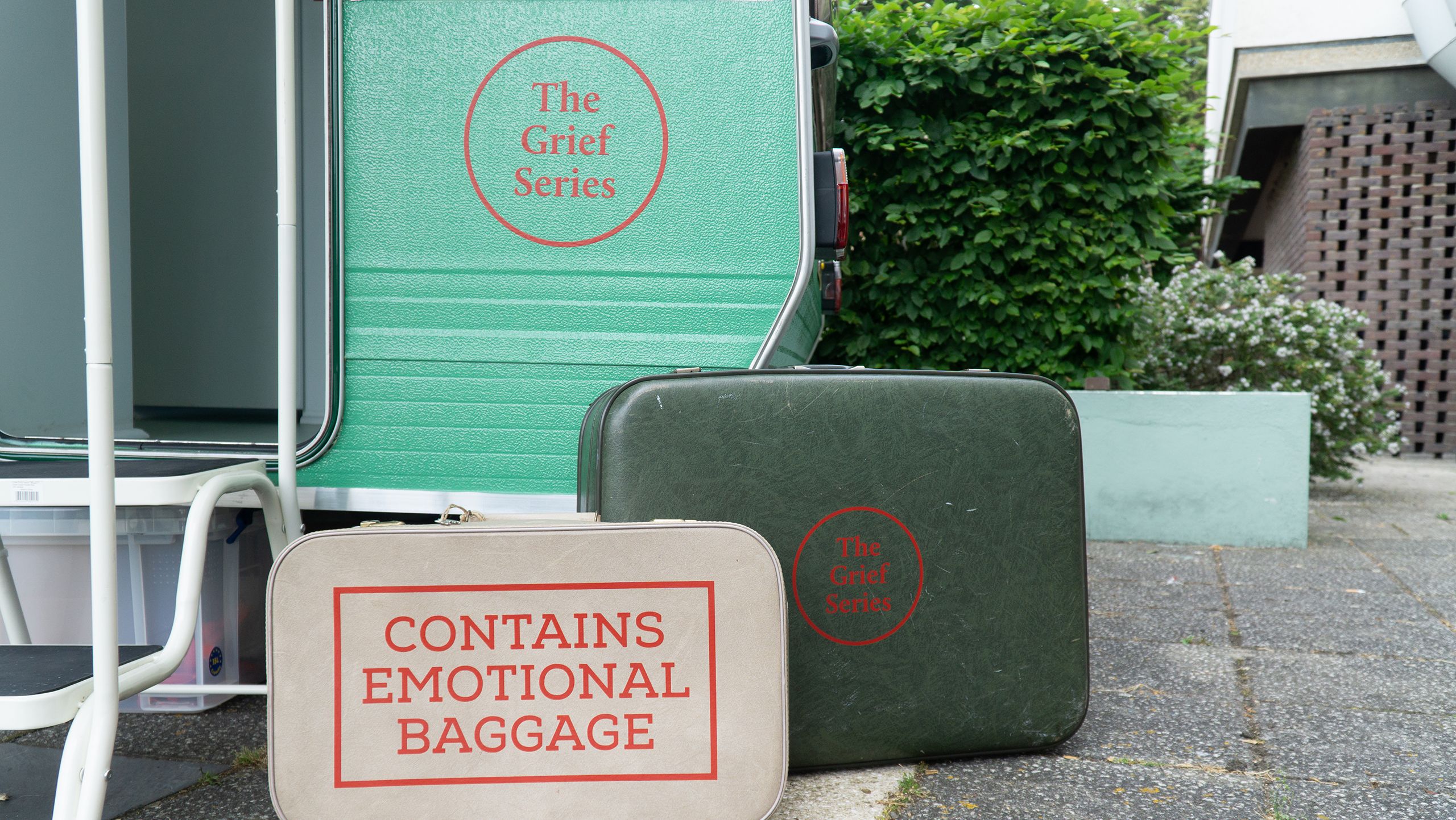 Suitcases outside a caravan used for 'Journey with Absent Friends'. One suitcase reads 'Contains emotional baggage'and the other 'The Grief Series'