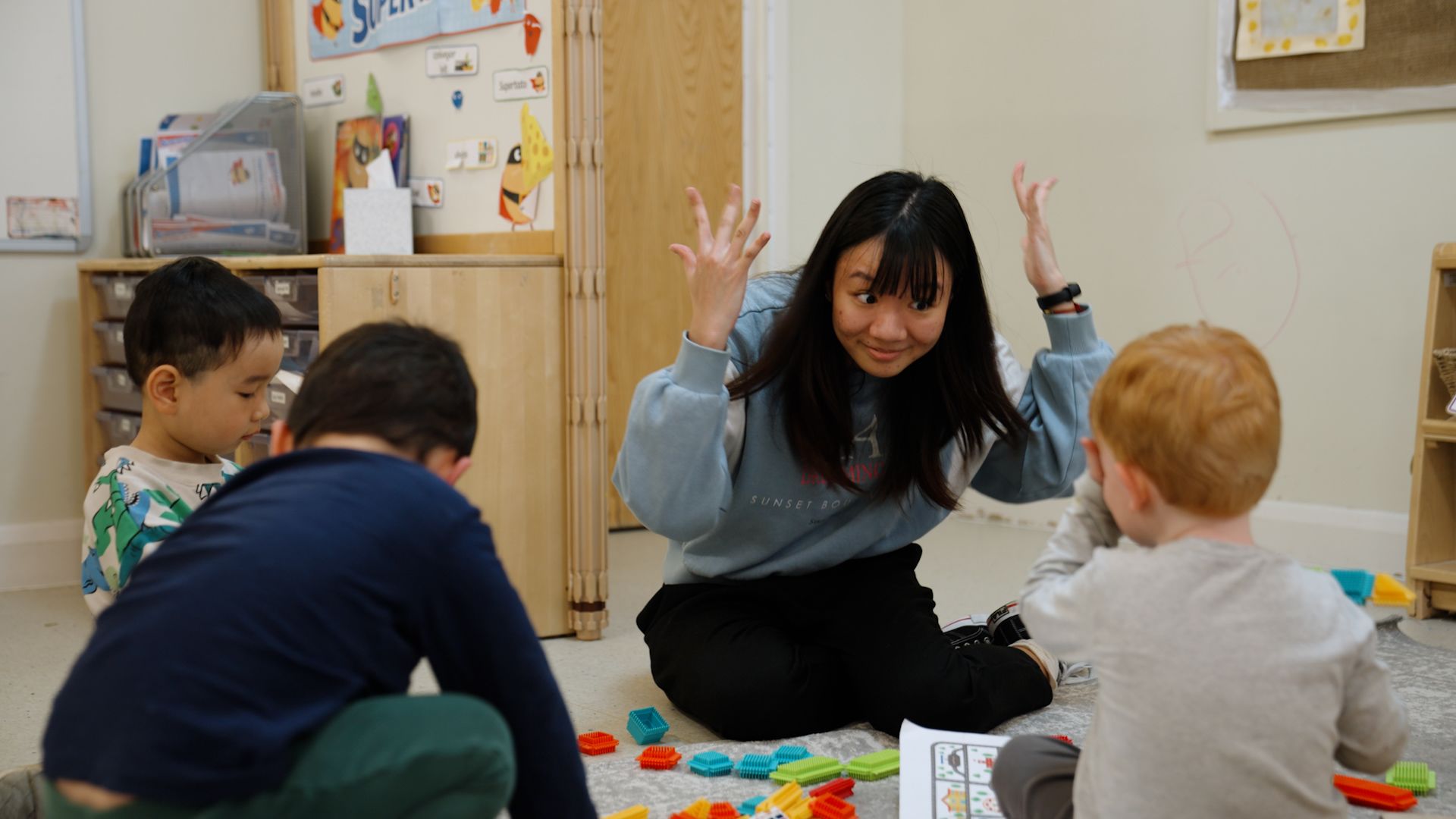 Hongqin You, sitting on the floor with three young children, making a playful gesture with their hands.