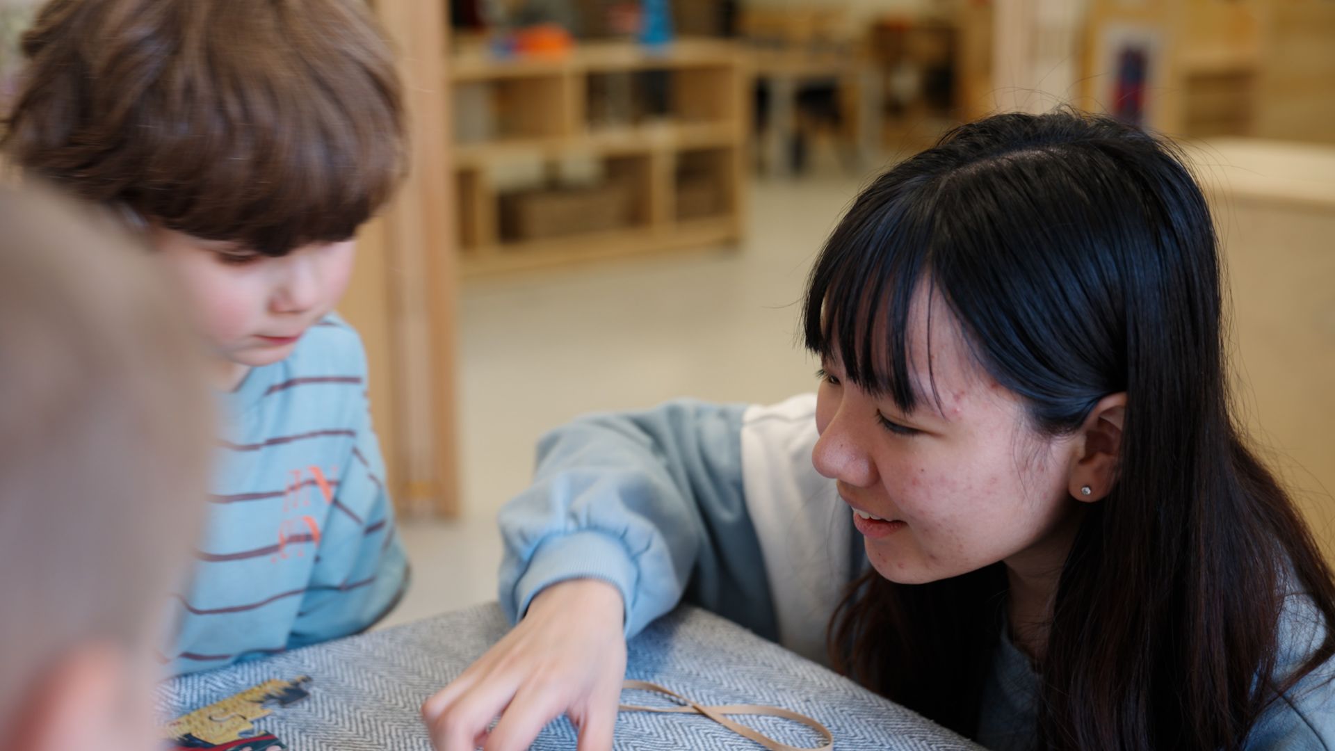 Hongqin You pointing to something on a table in front of a young child.