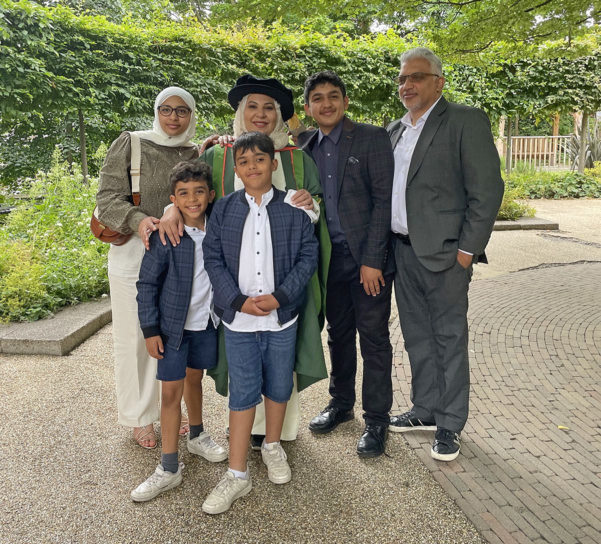 Shareefa surrounded by her children and family in front of a leafy hedge.