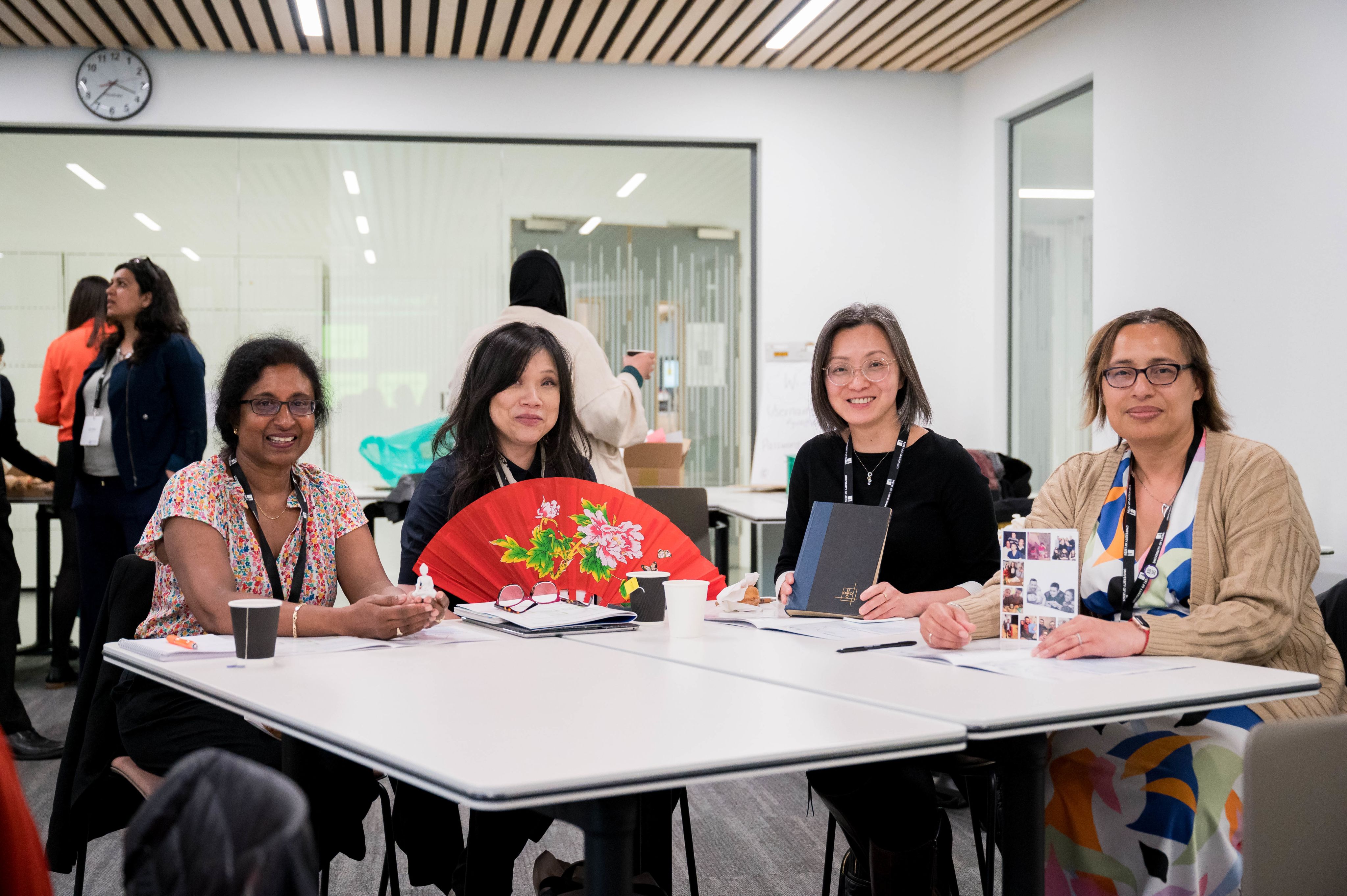 Four people sat at a table smiling. Sally is holding a large fan.