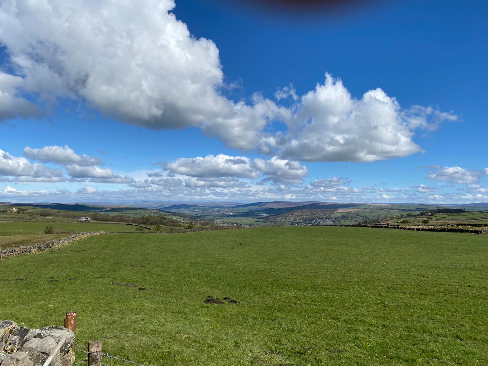 Green rolling hills with a blue sky and fluffy white clouds.