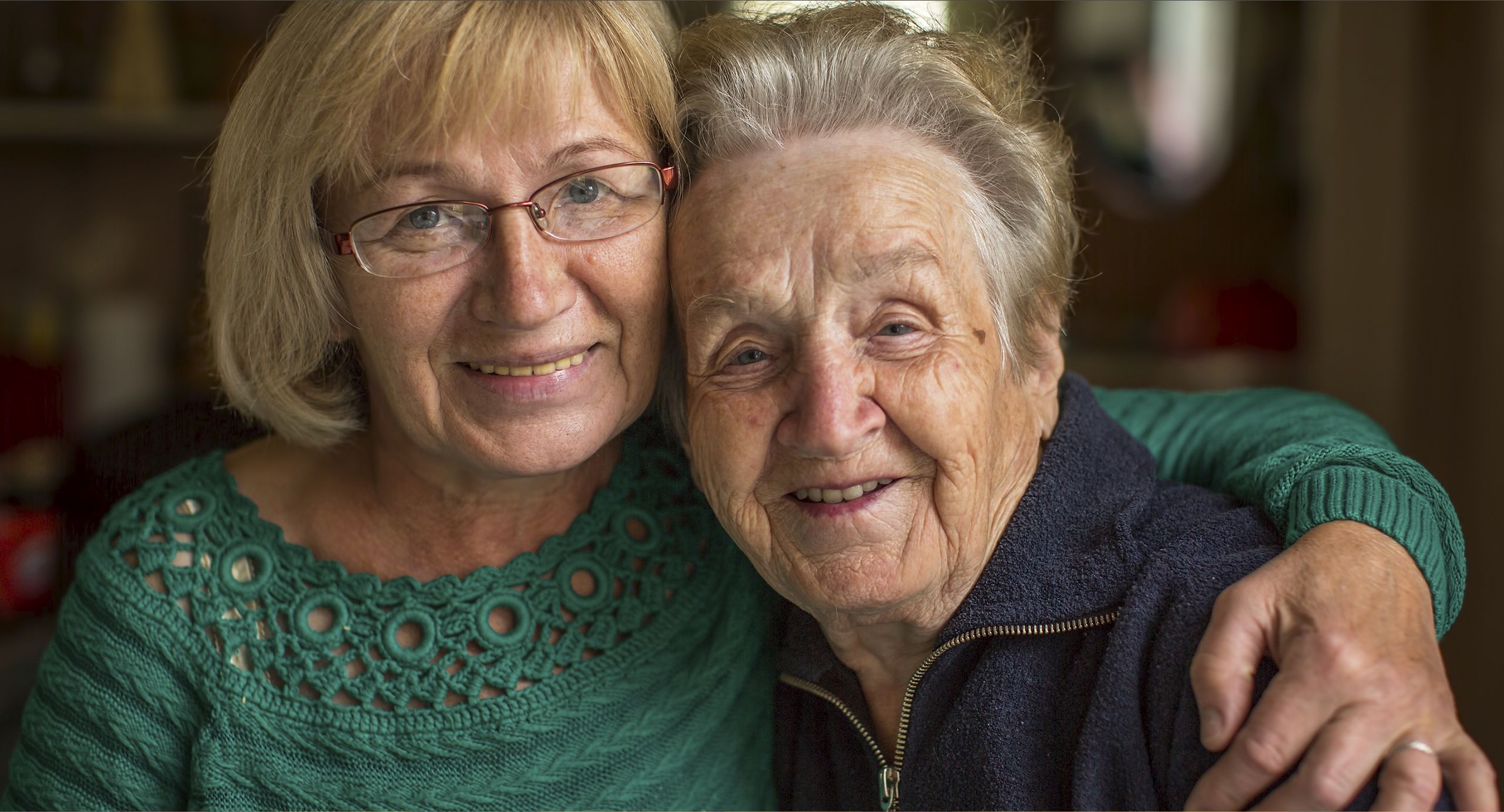 Two women smile at the camera. One has their arm around the shoulder of the other.