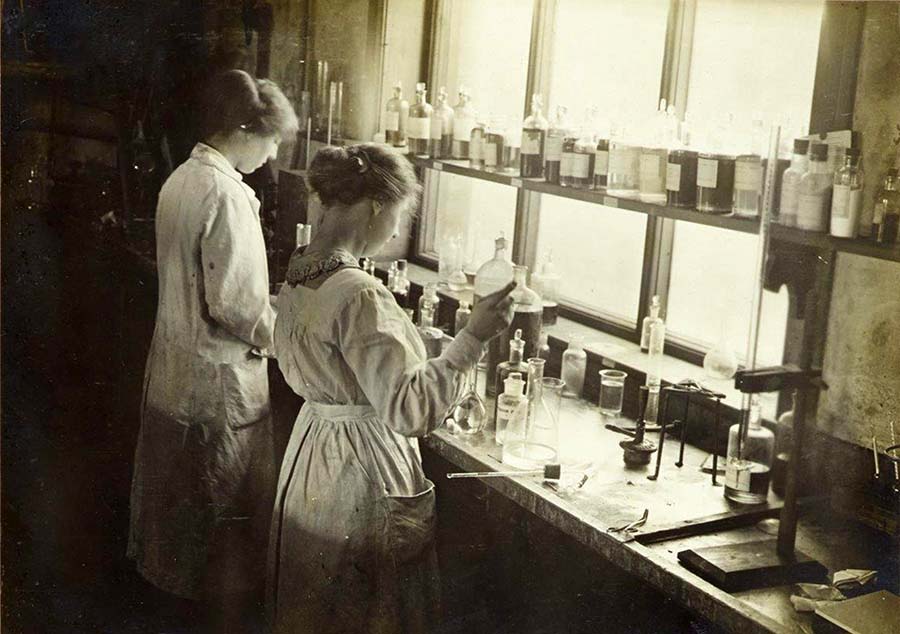 Black and white image of two female students facing away from camera working in laboratory