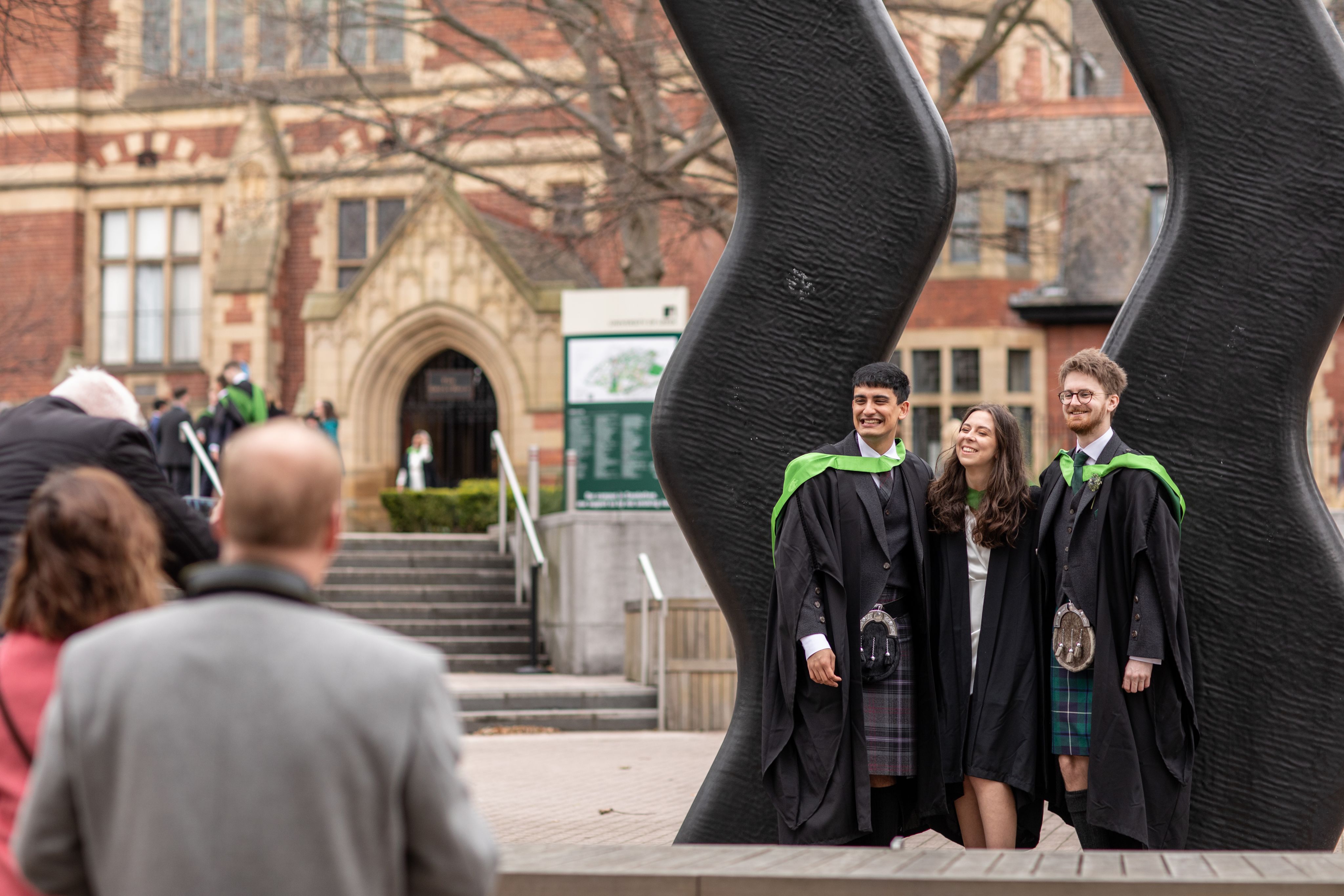 Students pose for photo in front of campus art on graduation day