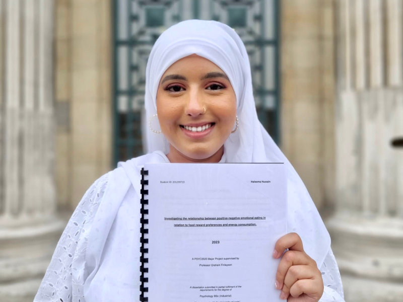 Haleema smiles on the Parkinson Steps holding her dissertation in hand