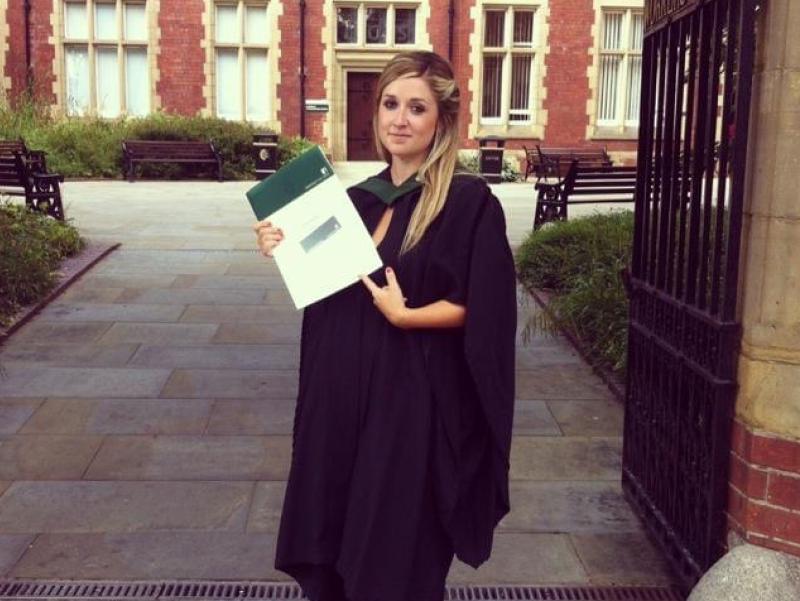 Rose stands with her graduation certificate on graduation day in Clothworkers Court