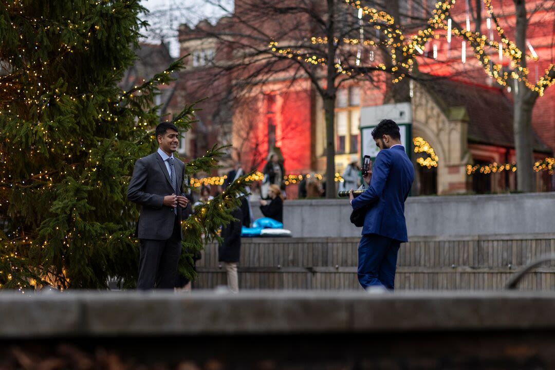 A graduate poses in front of a Christmas tree 