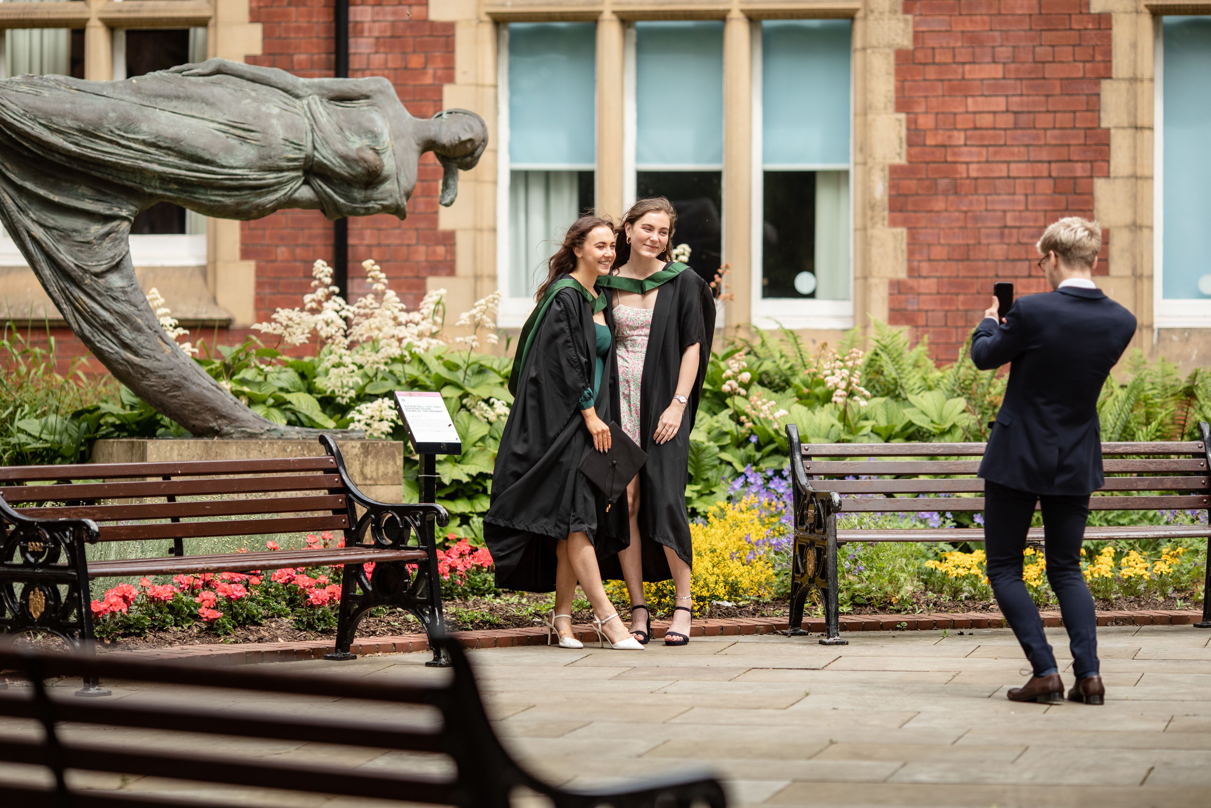 Two students pose in front of statue on campis