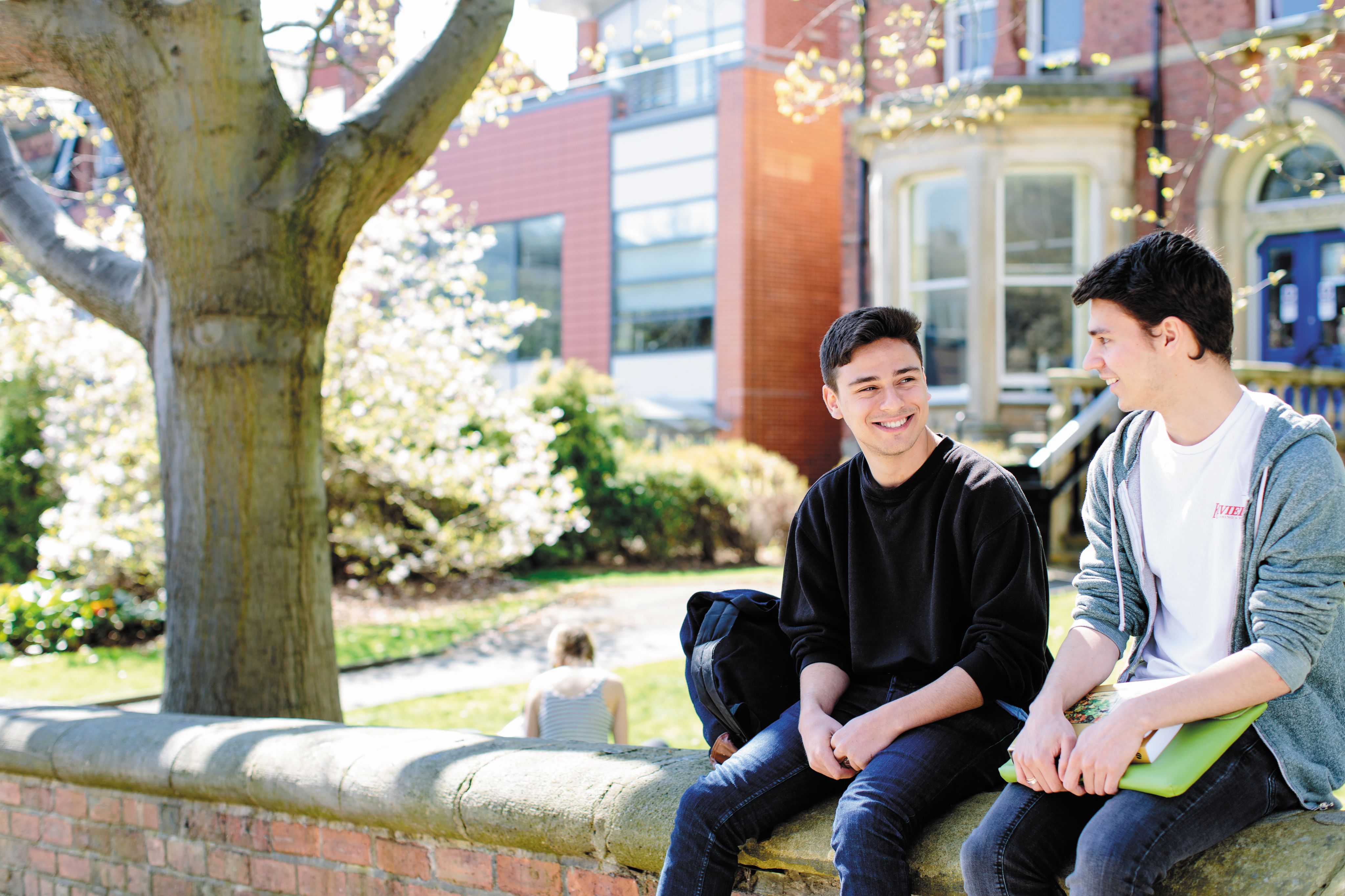 male students sat outside the school of english on wall 