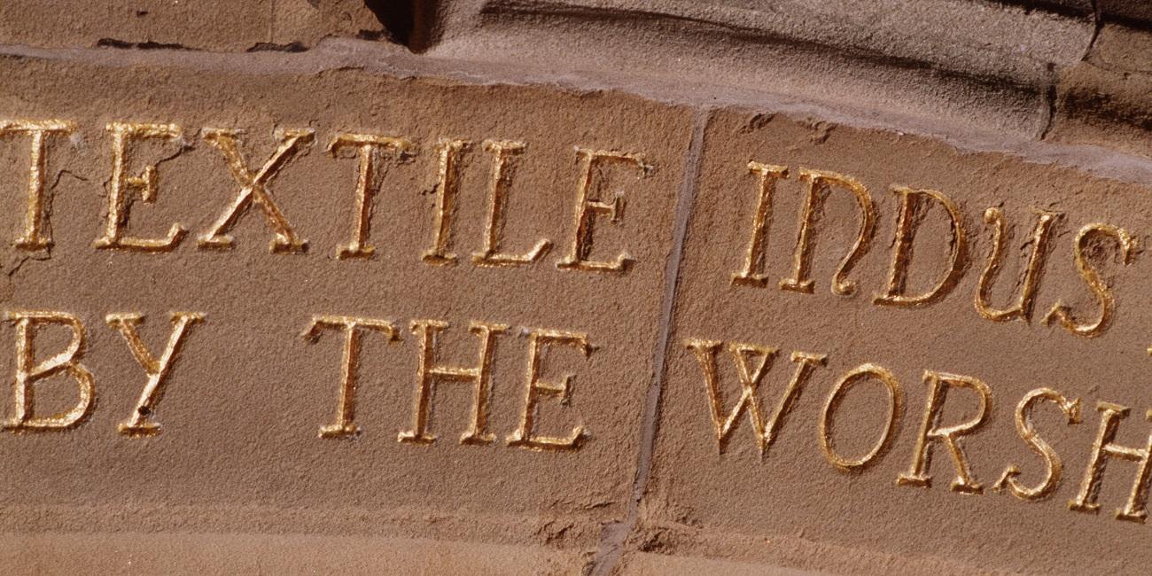 Words engraved in stone and painted gold. Part appears to read 'textile industries'.