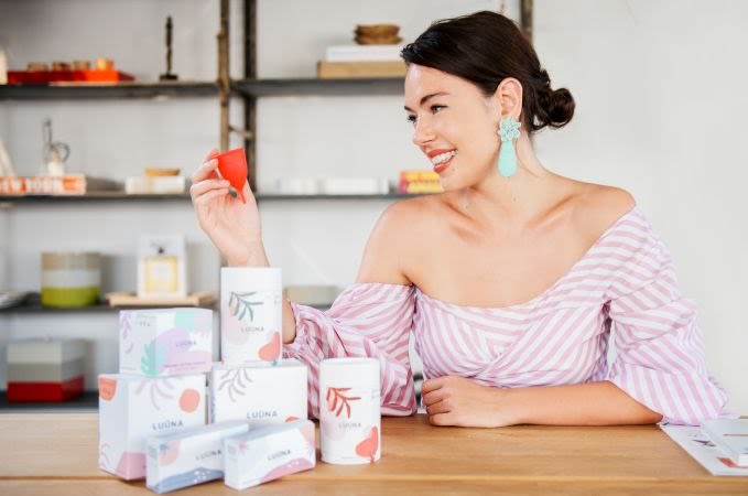 Olivia Cotes-Jones posing with her LUÜNA Naturals products. She is holding and looking at a menstrual cup
