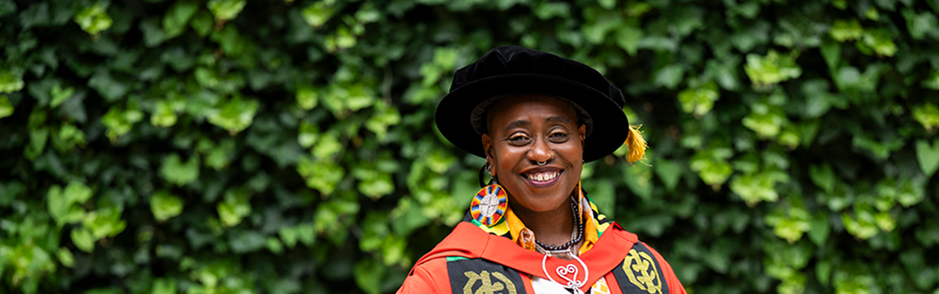 Khadijah in academic dress stood in front of greenery
