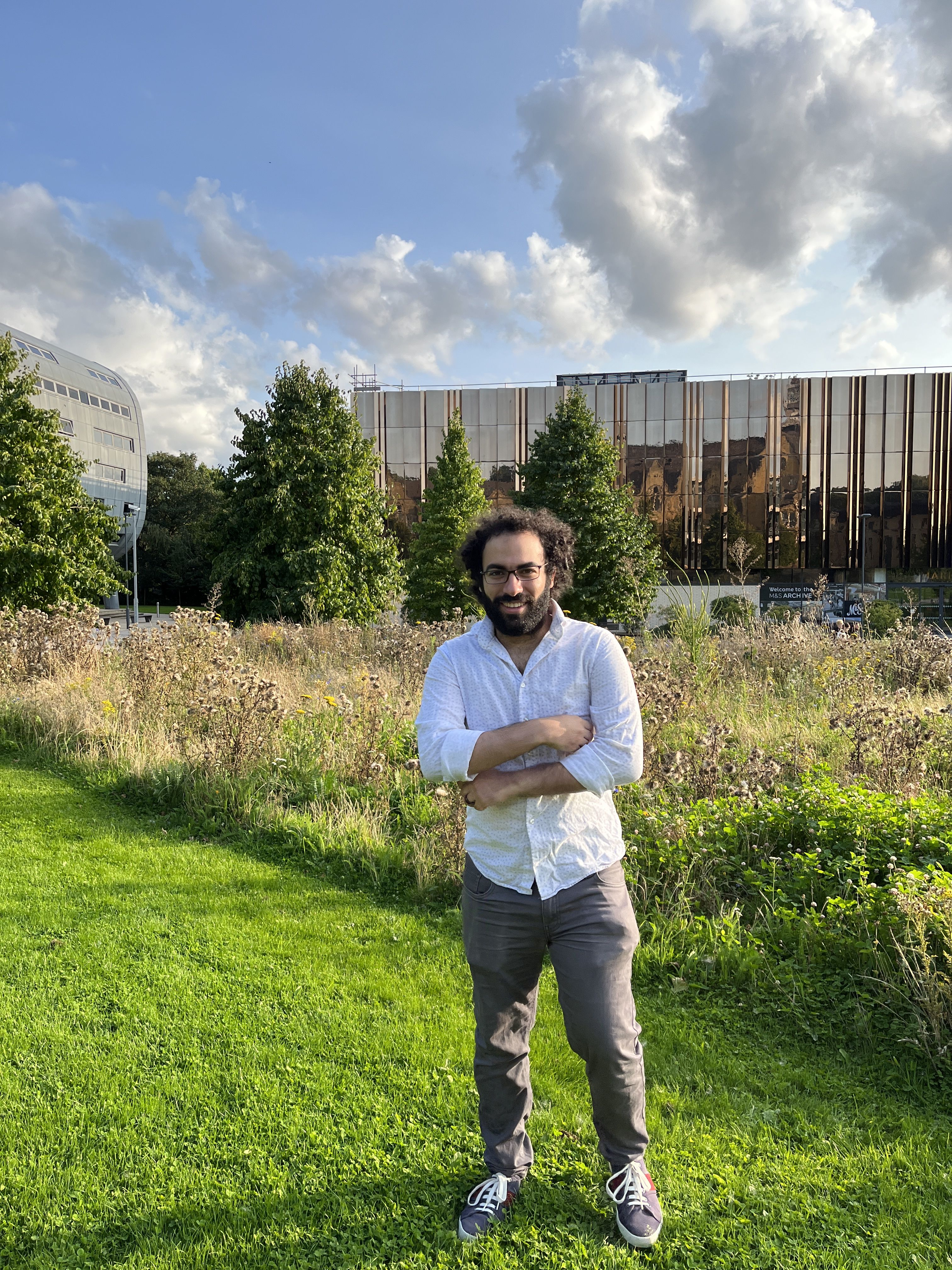 man standing with arms crossed in front of greenery