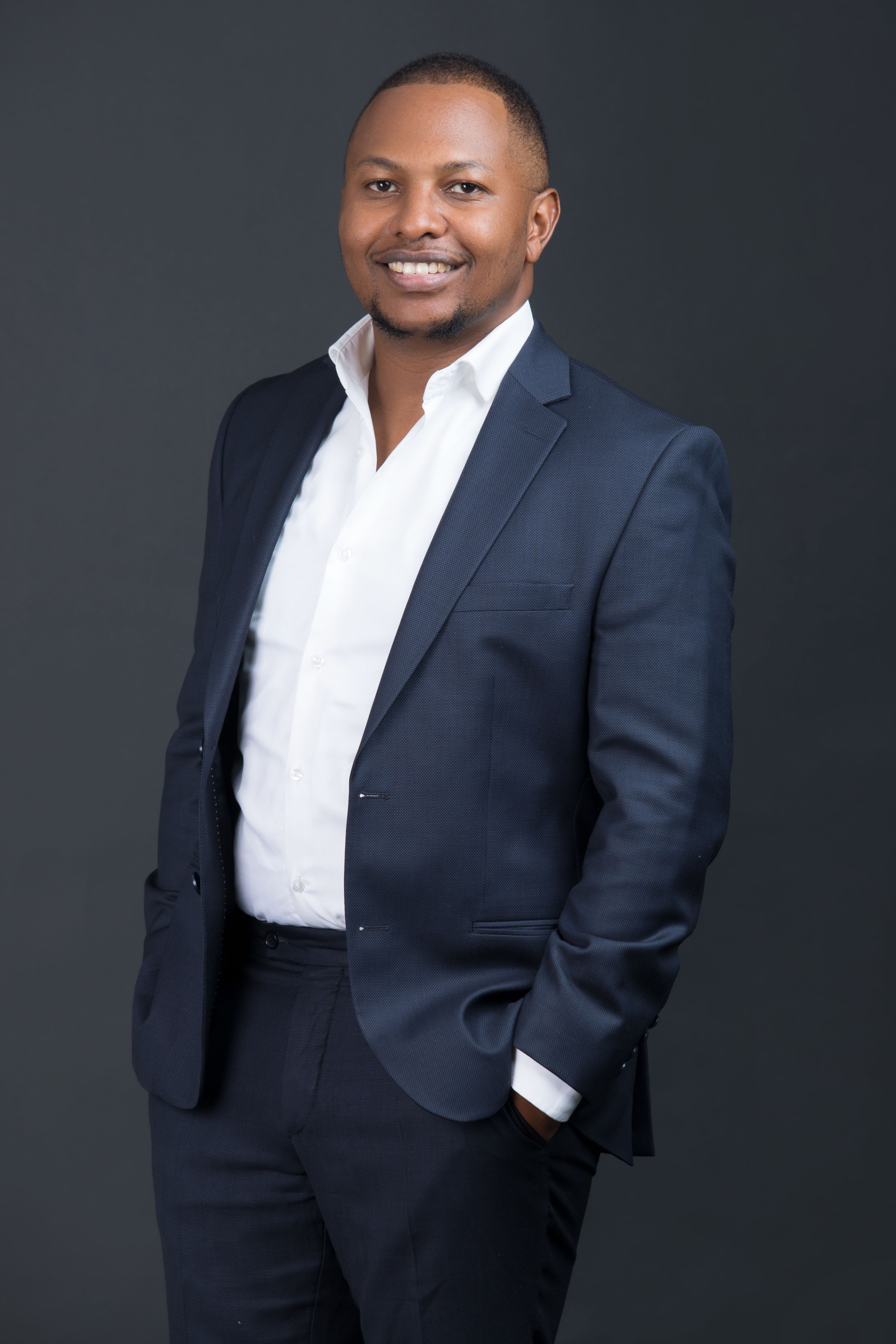 man in suit jacket with hands in pockets smiling at camera