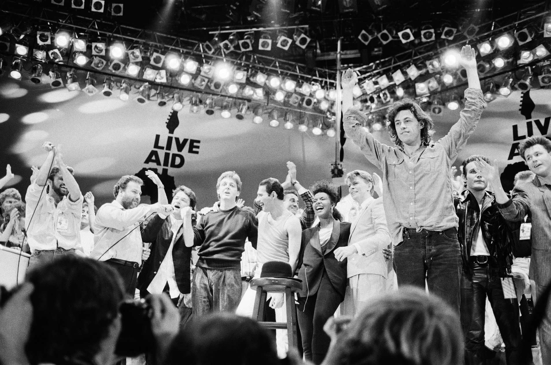 Bob Geldof on stage with many other music stars from Band Aid 1985. Bob raises his arms to acknowledge the crowd