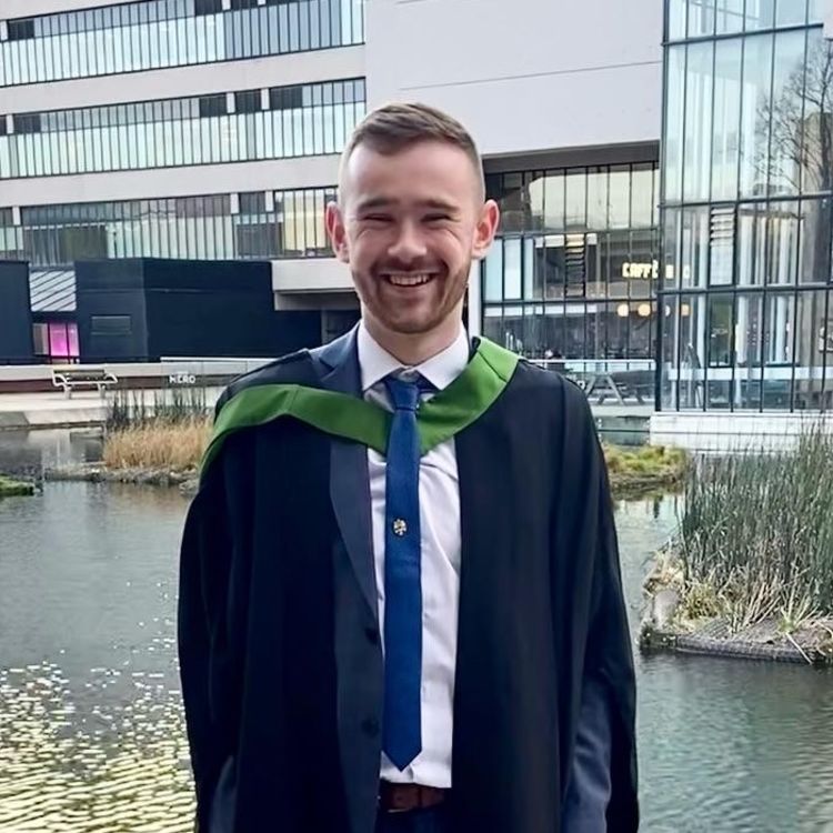 Lucas Warburton poses in front of Roger Steven's pond in his graduation gown
