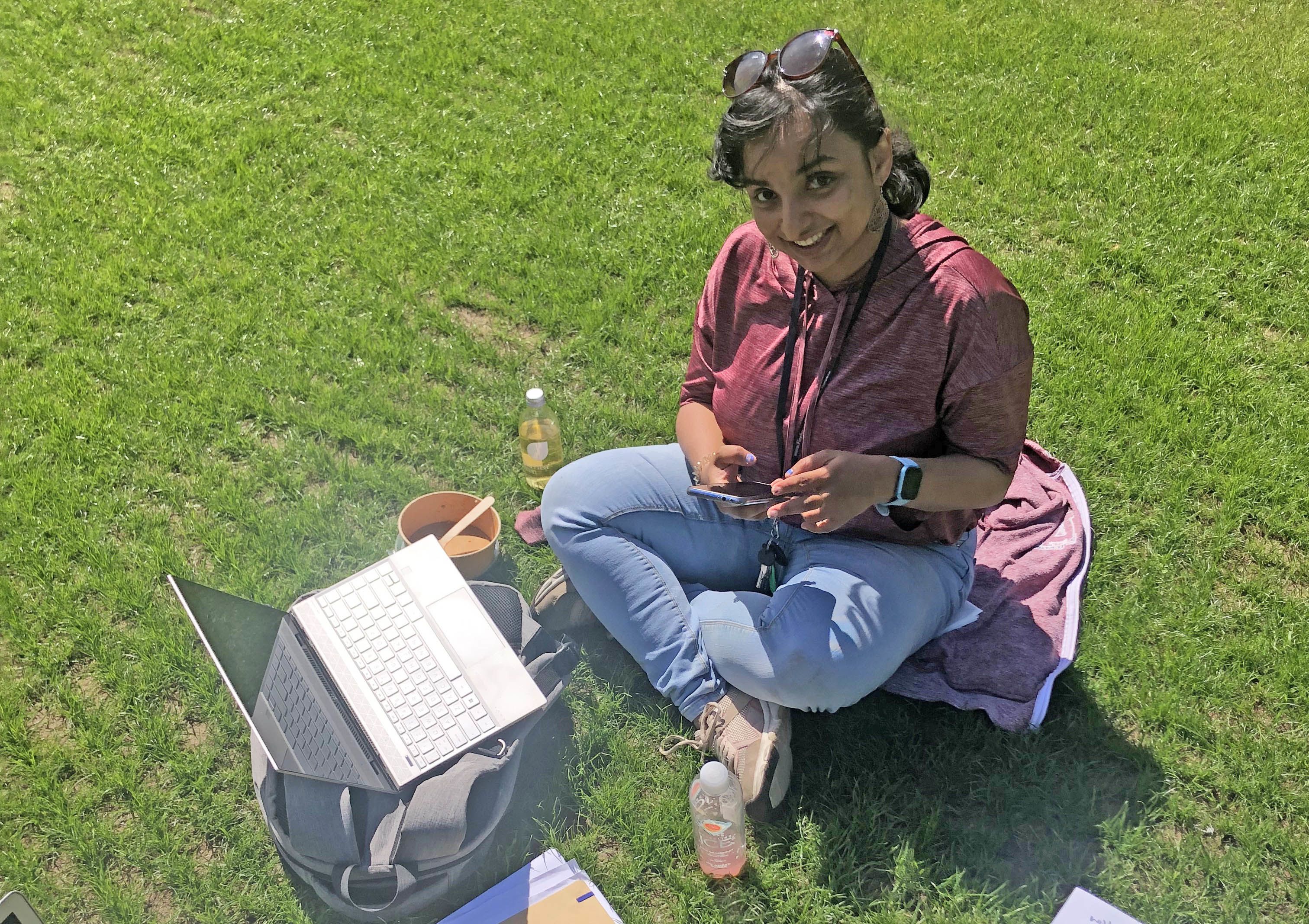 Merin pictured sat on the grass in a park with a laptop.