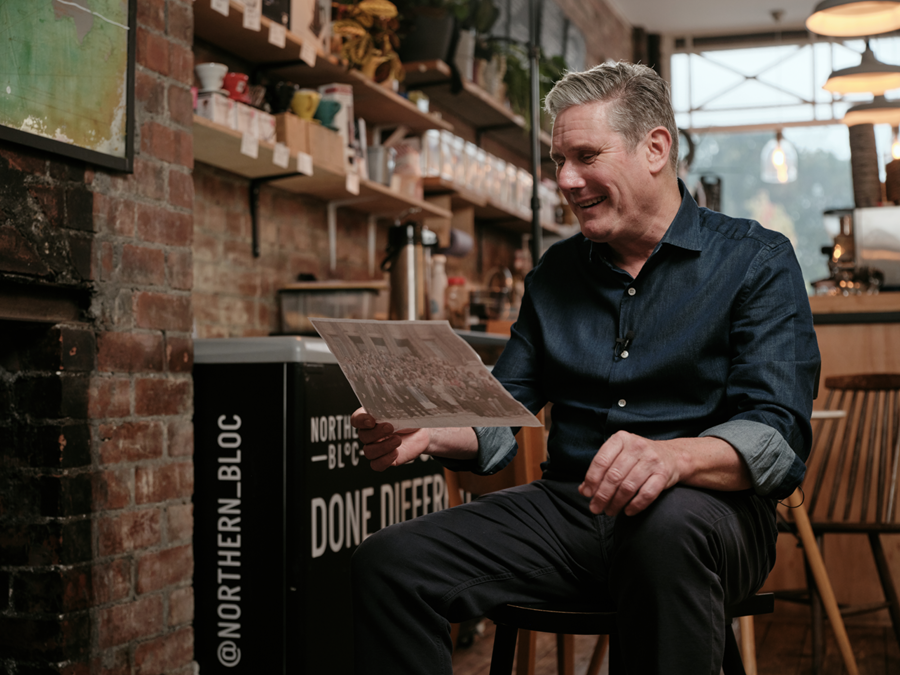 Keir Starmer sat on a chair in a bright, modern cafe bar, looking at an old photo of a class of students