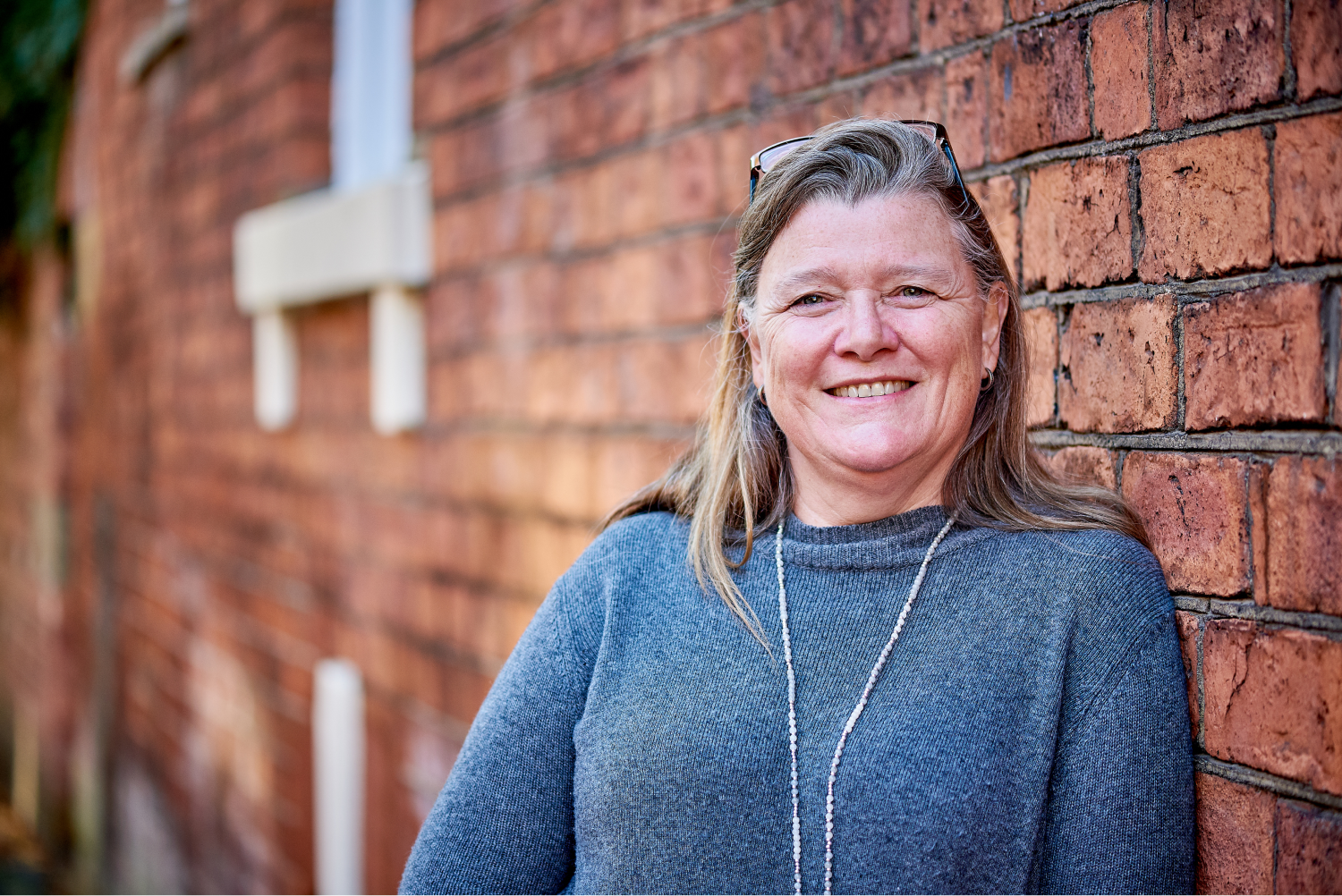 Profile image of a woman leaning against a red brick building