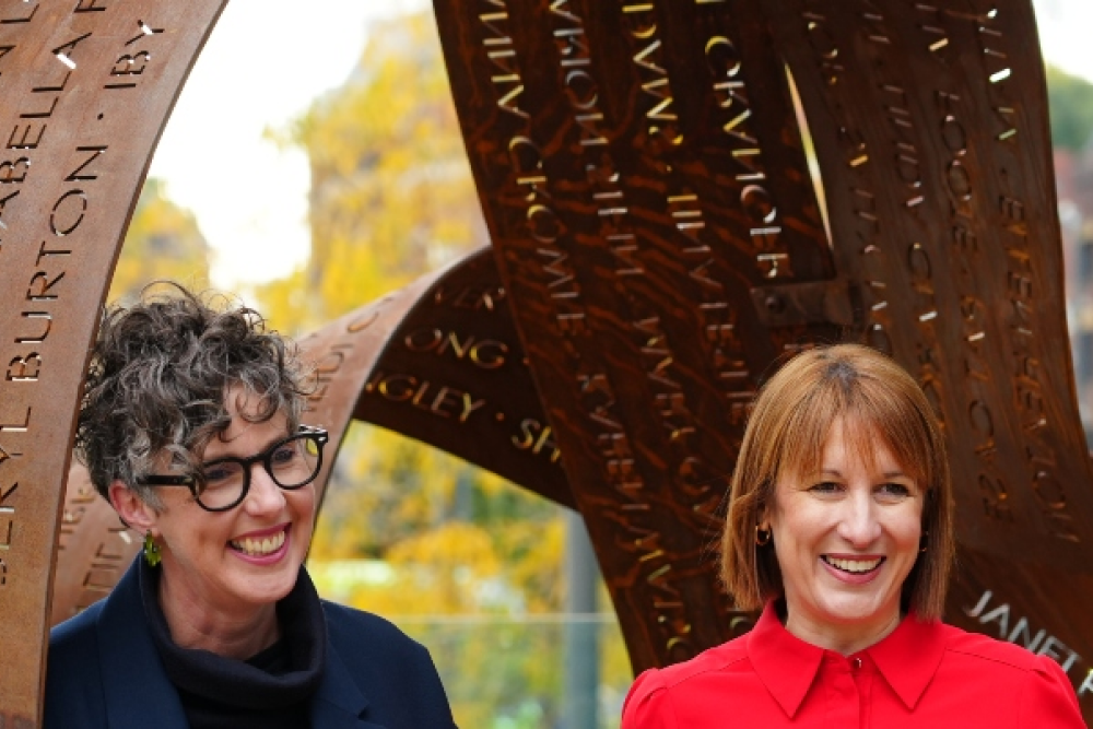 Two ladies smile in front of a sculpture