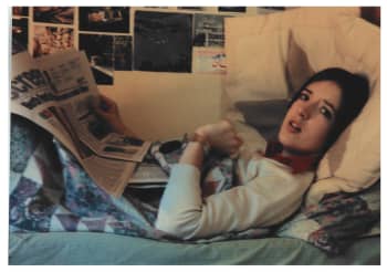 A student lies on a bed reading a newspaper