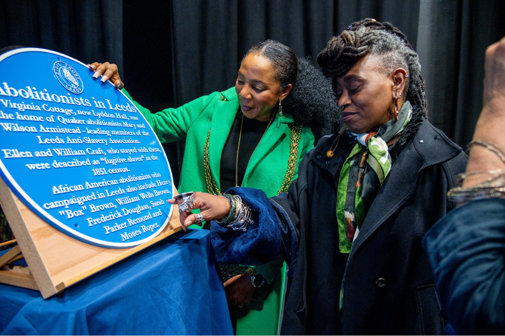 Two individuals look at a blue plaque