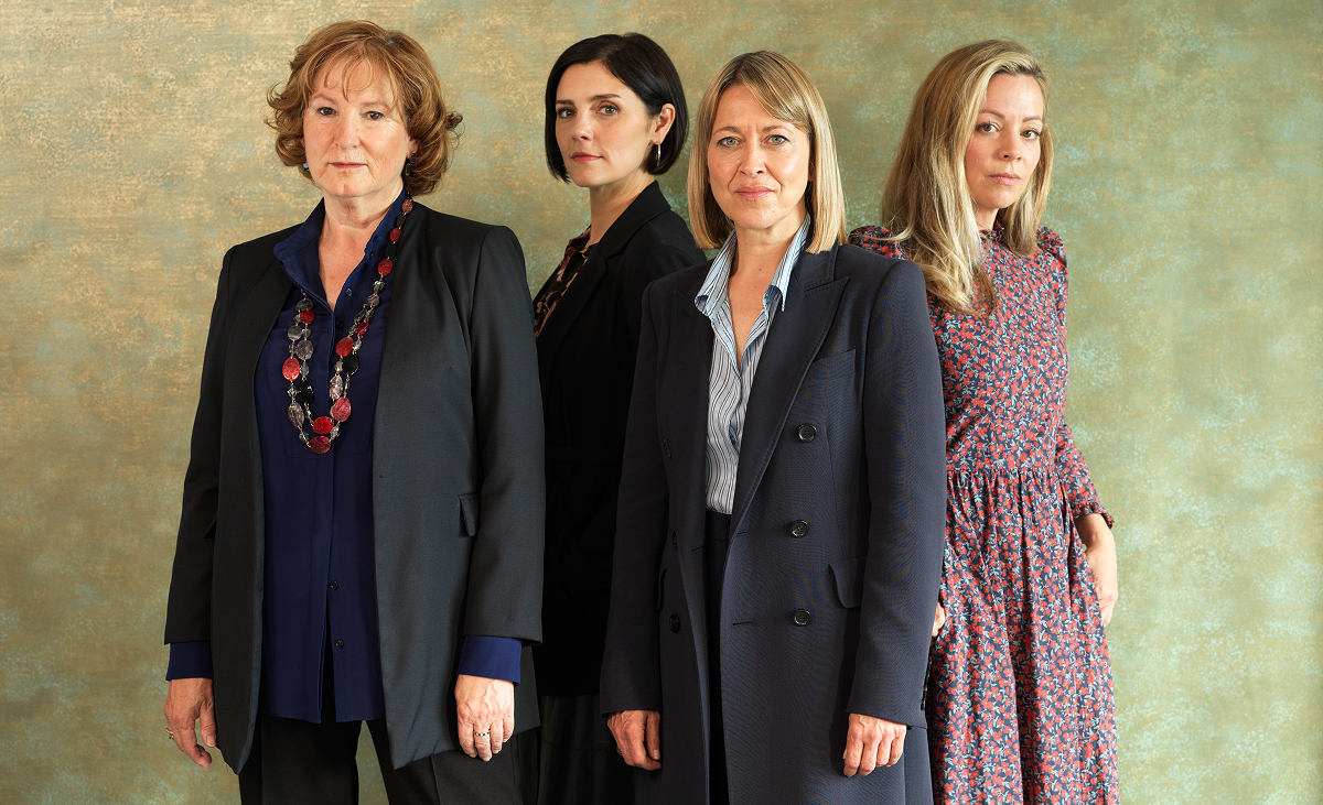 A group of four women pose for the camera in front of a blank background