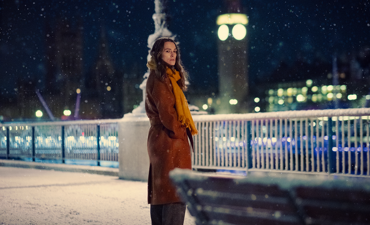 Keira Knightley stands on a bridge in London in the snow
