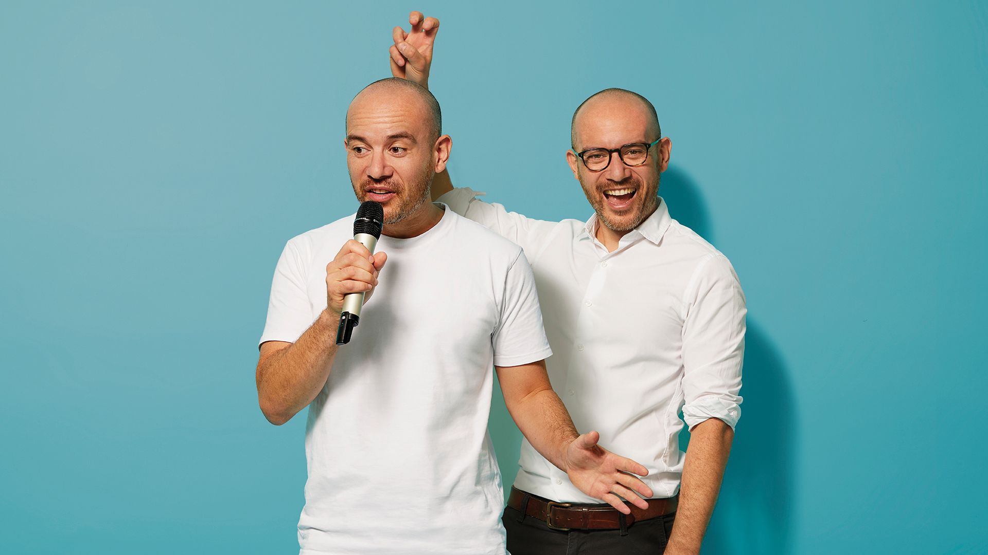 Tom Wong speaking into a microphone. Behind him, another image of Tom Wong wearing glasses makes a bunny ears gesture behind his head
