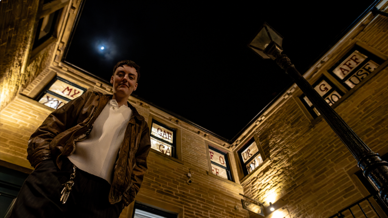 George Storm looks down the lens of the camera, and behind them artwork fills the windows of a stone building