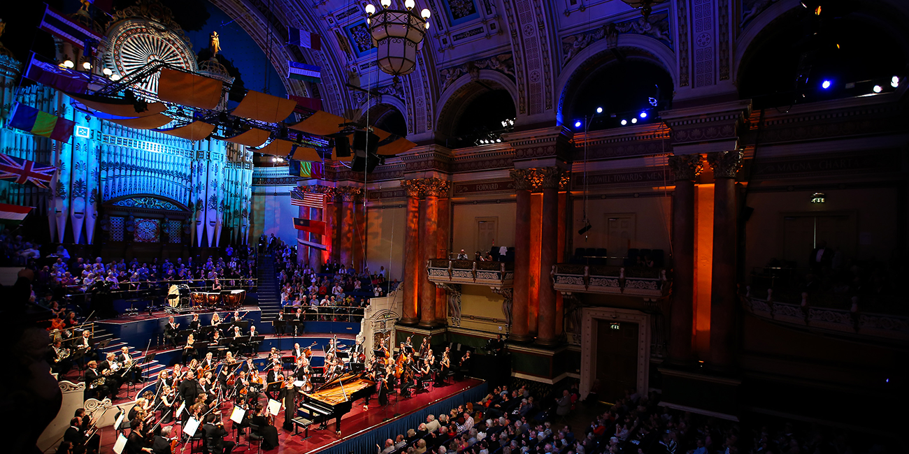 An orchestra and pianist on stage at Leeds Town Hall. Red and blue lights illuminate the high walls and ceiling.
