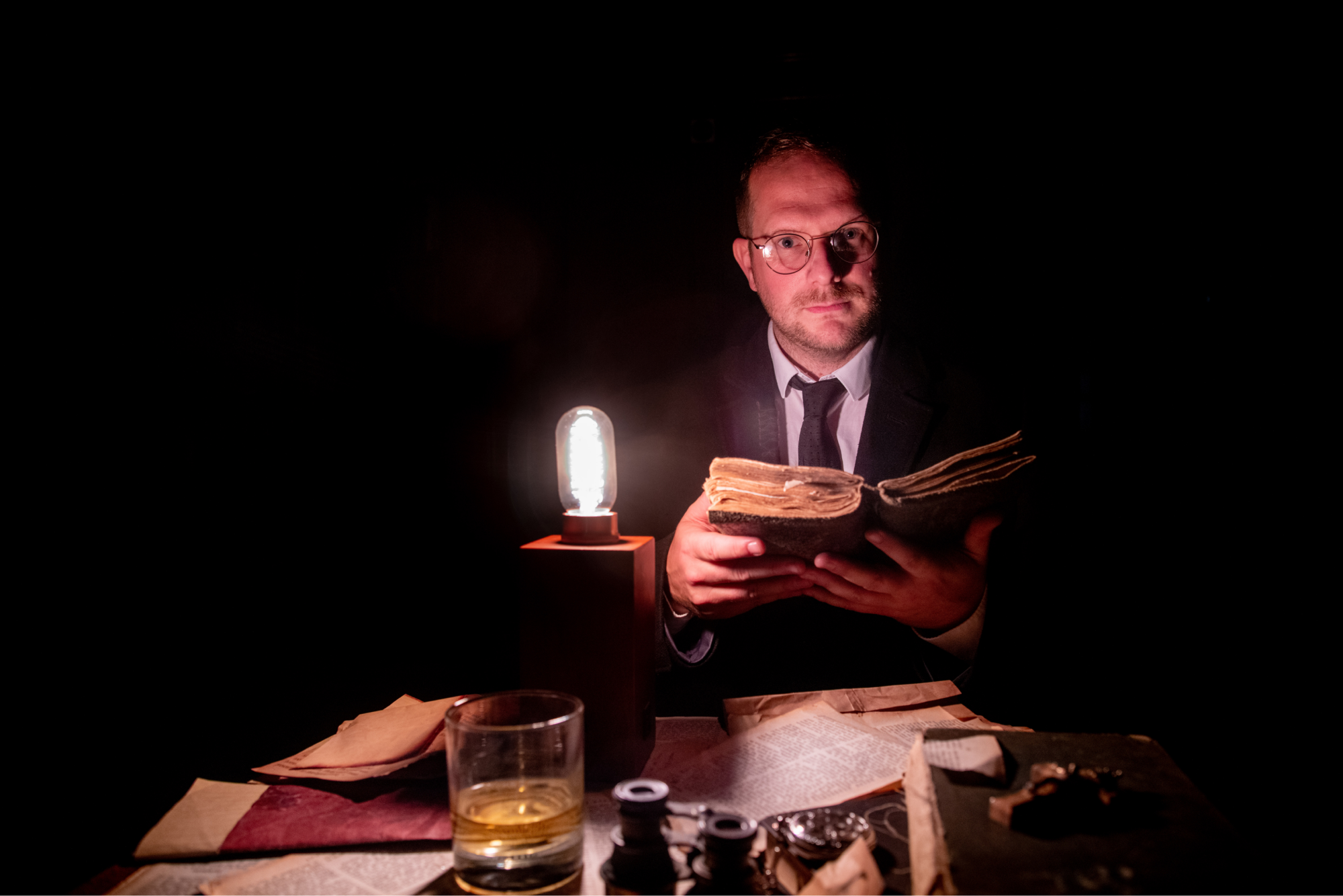 Storyteller lit by a lantern holds an old book before him as her prepares to tell a story