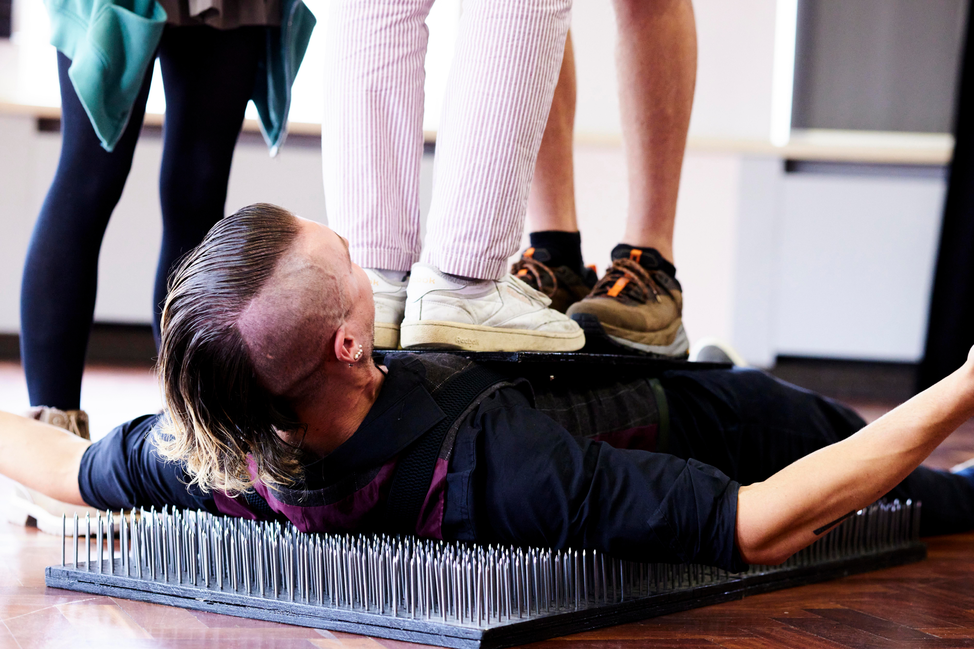 Performer lies on a bed of nails with two students stood upon his chest