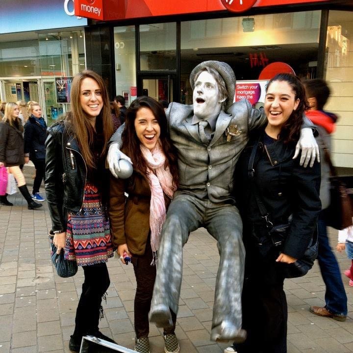 Three woman pose for a photo with a street performer, who is covered in silver paint