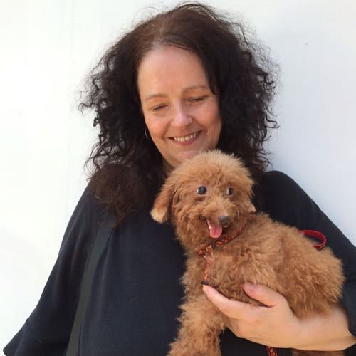 Photo of a woman with dark curly hair holding a dog with ginger hair