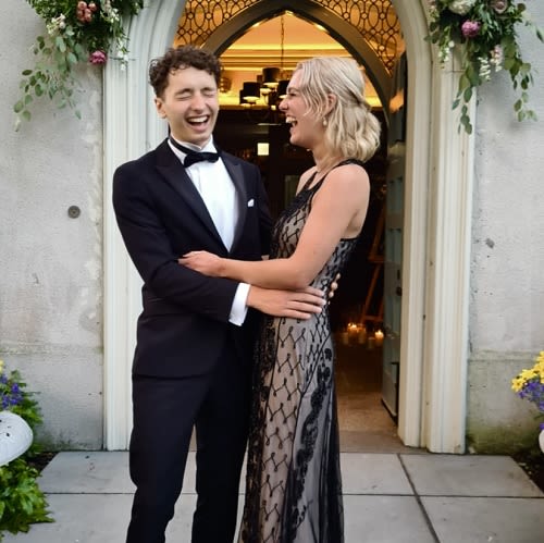 A man in a tuxedo and a woman in a dress embrace and are captured mid-laughing