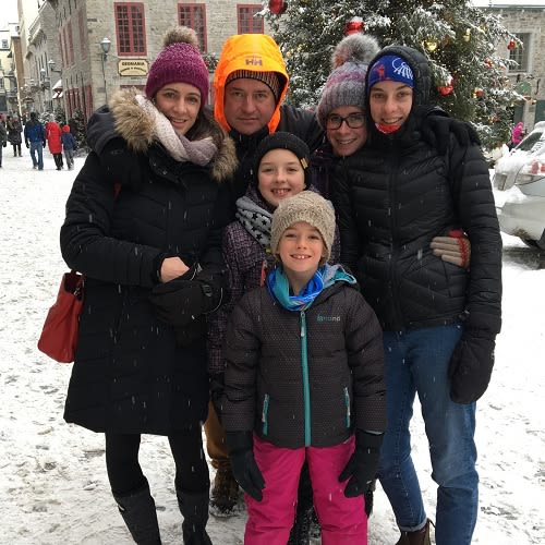 A family of 6 pose in the snow, wearing warm clothing, hats and gloves