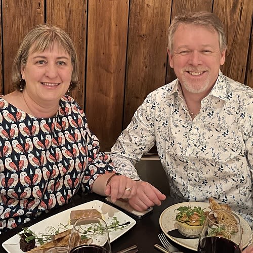A couple posing for a photograph sat at a restaurant table with food in front of them.