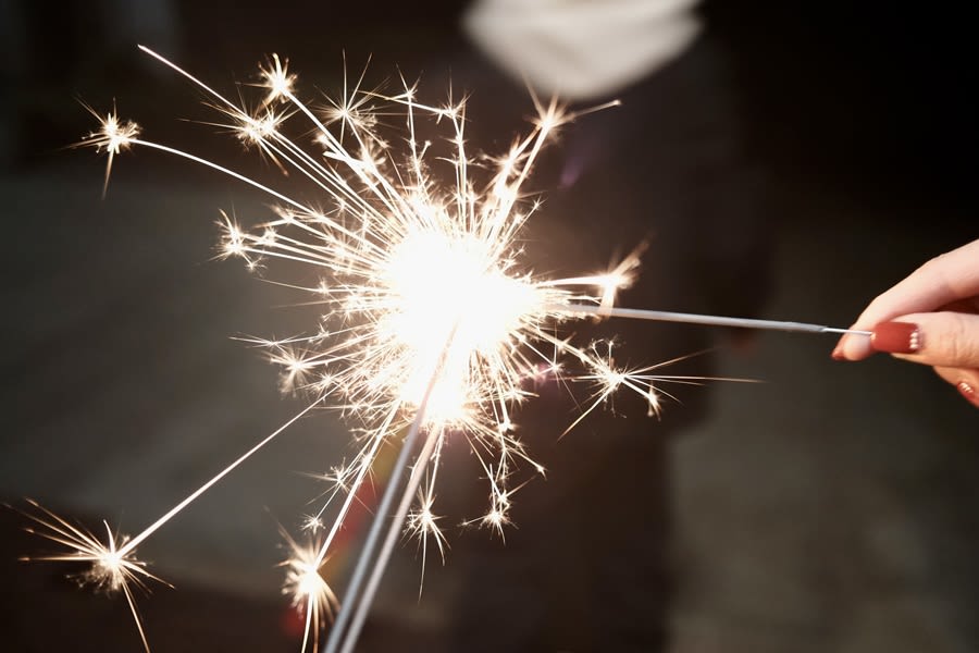 A person's hand lighting a sparkler firework which has bright sparks coming off it