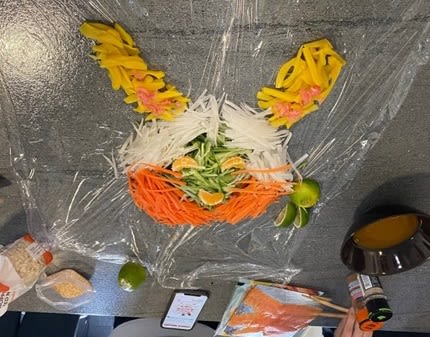 A selection of sliced vegetables laid out to form a representation of a rabbit's head. Next to it are ingredients and condiments